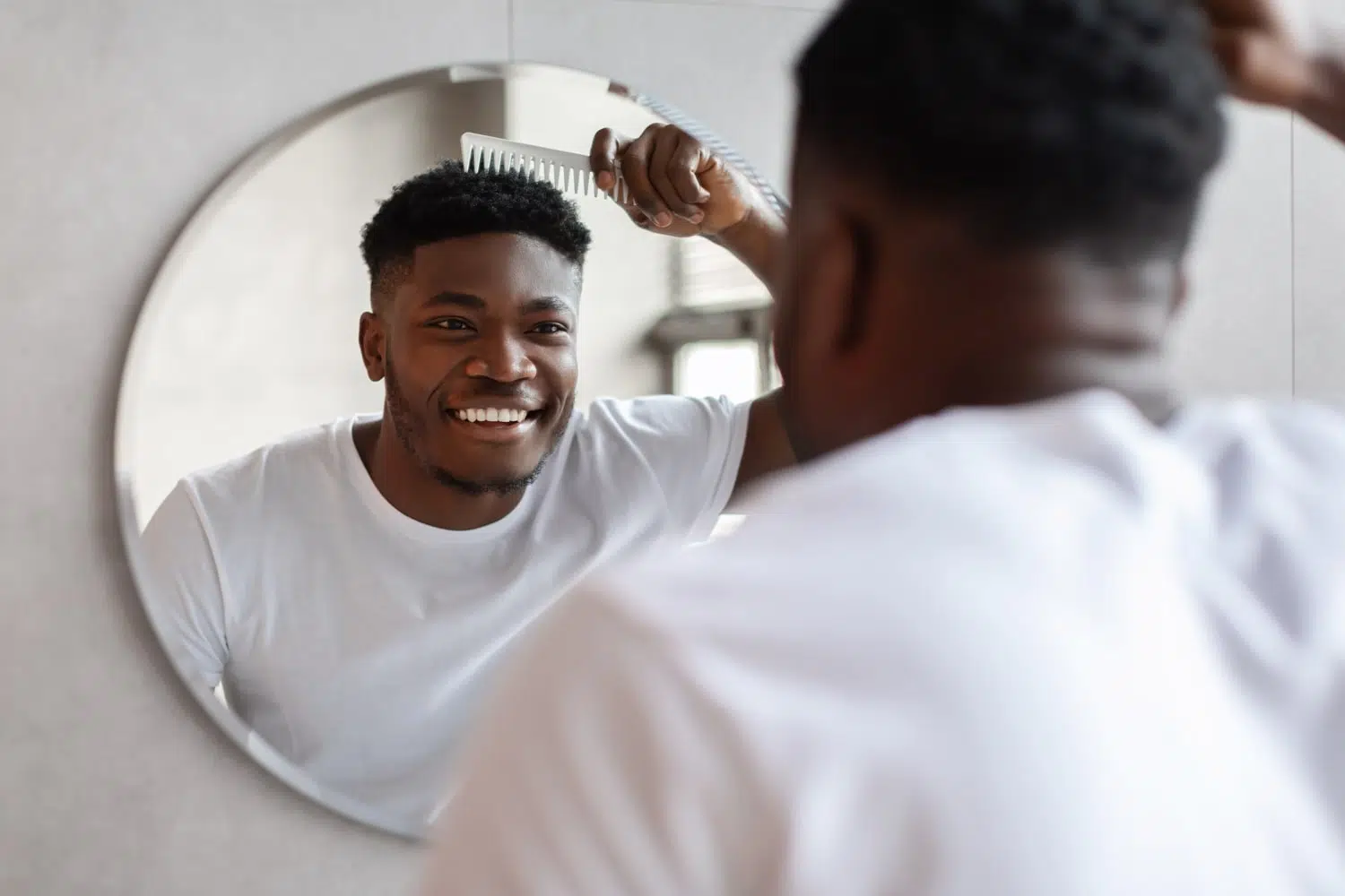 Smiling individual with short afro-textured hair styling in front of a mirror, reflecting confidence after a successful Afro Hair Transplant Turkey